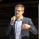 Referent im Anzug mit Mikrofon spricht über Holzbauausschreibung und Bau-Ausschreibungen